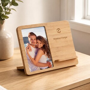 May include: A rectangular bamboo wireless charger stand featuring a vertical photo frame on the left side and a charging pad area on the right. The wood surface displays a circular charging icon and the text Wireless Charger printed in black.