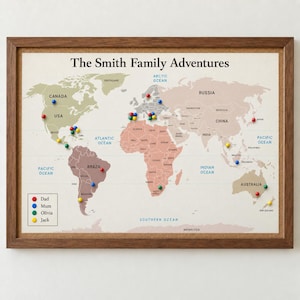 May include: A framed world map titled The Smith Family Adventures with a cork backing. The map features muted earth tones and is populated with red, blue, green, and yellow push pins. A legend in the bottom left corner identifies the pins by name.