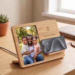 May include: A bamboo wireless charger with a photo frame. The frame holds a family photo. A black smartphone rests on the charger, displaying the time. The charger is on a wooden surface.