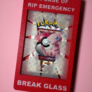 May include: A rectangular red glitter frame with the text IN CASE OF RIP EMERGENCY at the top and BREAK GLASS at the bottom. The center features a clear, textured plastic insert designed to look like shattered glass, holding a Pokemon trading card pack.