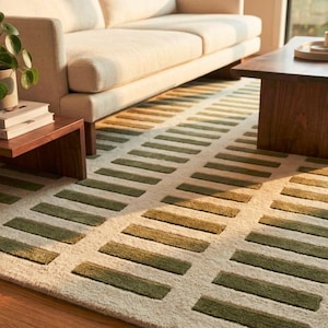 May include: A rectangular area rug featuring a cream-colored base with a repeating pattern of dark olive green horizontal rectangular blocks arranged in parallel rows, creating a textured geometric design across the entire surface of the rug.
