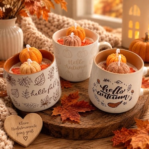 Könnte beinhalten: Drei Keramikbecher gefüllt mit Wachs, jeweils mit kleinen kürbisförmigen Kerzen verziert. Die Becher zeigen herbstliche Illustrationen von Blättern, Pilzen und Kürbissen sowie die Aufschriften "hello fall" und "hello autumn".