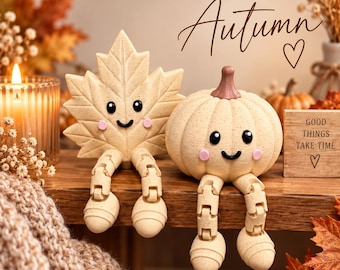May include: Two beige decorative figures with articulated legs, one shaped like a maple leaf and one like a pumpkin, both featuring black eyes, a smiling mouth, and pink cheeks. A wooden sign nearby displays the text Good Things Take Time.
