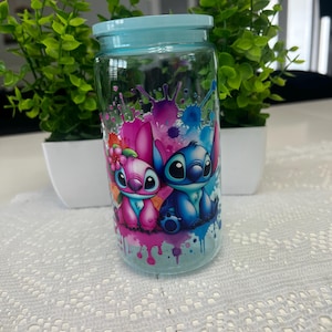 Puede incluir: Un tarro de cristal transparente con tapa azul claro, con un gr&aacute;fico colorido de dos personajes de dibujos animados. El tarro est&aacute; decorado con salpicaduras de pintura rosa, azul y morada. El tarro est&aacute; sobre un mantel de encaje blanco.
