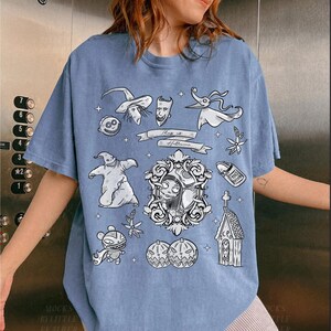 Puede incluir: Camiseta azul claro con ilustraciones en blanco y negro de la pel&iacute;cula "Pesadilla antes de Navidad". El dise&ntilde;o incluye personajes como Jack Skellington, Sally y Zero, junto con el texto "This is Halloween".
