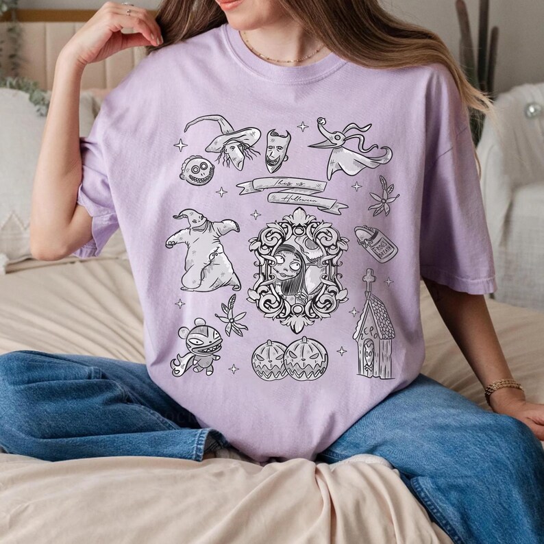 Puede incluir: Una camiseta de color lila claro con ilustraciones en blanco y negro de personajes y objetos de "Pesadilla antes de Navidad". El dise&ntilde;o incluye a Jack Skellington, Sally, Zero y otros elementos tem&aacute;ticos de Halloween. La camiseta tambi&eacute;n tiene el texto "This is Halloween."