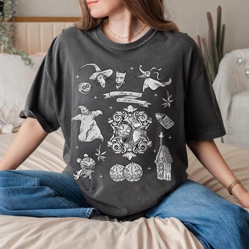 Puede incluir: Camiseta gris oscuro con ilustraciones en blanco y negro de una pel&iacute;cula tem&aacute;tica de Halloween. El dise&ntilde;o incluye personajes, calabazas y el texto "This is Halloween" en una pancarta. La camiseta tiene mangas cortas y un corte holgado.