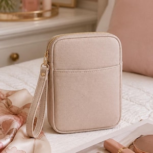 May include: A rectangular beige wristlet pouch with a smooth fabric texture, a gold-toned zipper closure, and a matching wrist strap. The pouch features a front slip pocket and a structured, rounded-edge design, providing a compact storage solution.