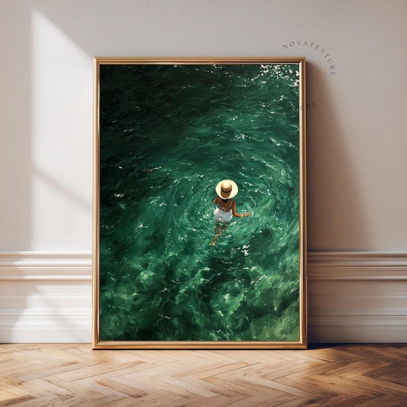 May include: A framed wall art print featuring a high-angle view of a person wearing a white swimsuit and a straw hat, floating in deep emerald green water. The water surface shows ripples and light reflections, with the text NOVATEXTURE visible.