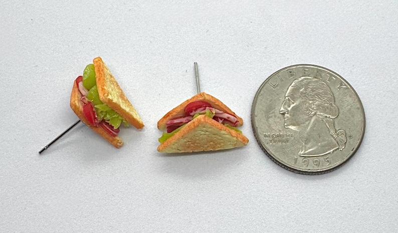 Pu&ograve; includere: Mini sandwich con ripieni di lattuga, pomodori e altri ingredienti, tenuti insieme con stuzzicadenti. Una moneta da un quarto di dollaro USA &egrave; accanto ai panini per il confronto delle dimensioni. I panini sono su una superficie bianca.