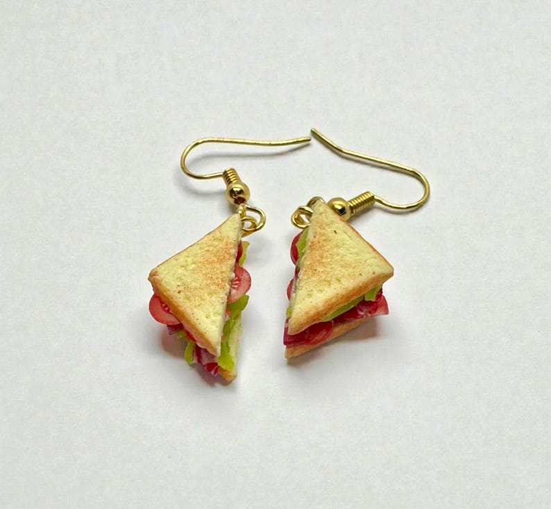 Pu&ograve; includere: Un paio di orecchini a forma di triangoli di sandwich in miniatura. Gli orecchini hanno fili per le orecchie dorati e sono progettati per assomigliare a pane tostato, lattuga e ripieni di pomodoro. Un accessorio divertente e stravagante.