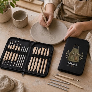 May include: A black zippered case containing a set of wooden and metal pottery sculpting tools, with a matching black case featuring an illustration of an apron and the name SOPHIA. The tools include various shapes for carving clay.
