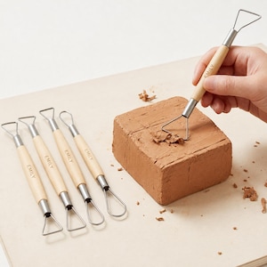 May include: A set of five clay sculpting tools with light wood handles, each featuring the name EMILY engraved on the side. The tools have metal wire loops in various shapes at the ends, and one tool is shown carving into a block of brown clay.