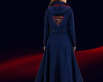 Puede incluir: Abrigo largo azul marino con capucha y falda acampanada. La parte trasera del abrigo presenta el logotipo de Superman dorado y rojo. La capucha tiene una franja roja. El abrigo tiene dos botones en la cintura.