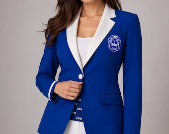 Puede incluir: Una blazer azul real con cuello y puños blancos. La blazer presenta un escudo blanco en el pecho y las letras ZΦB. Se abrocha con un solo botón blanco. La modelo lleva pantalones blancos.