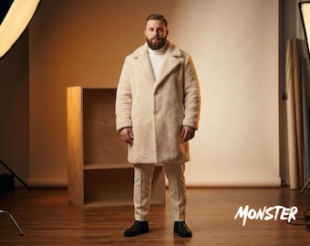 Puede incluir: Un abrigo de piel sintética color crema con solapa de muesca y cierre de un solo botón, usado sobre un suéter de cuello alto blanco y pantalones color crema. La palabra MONSTER está impresa en blanco en la esquina inferior derecha.