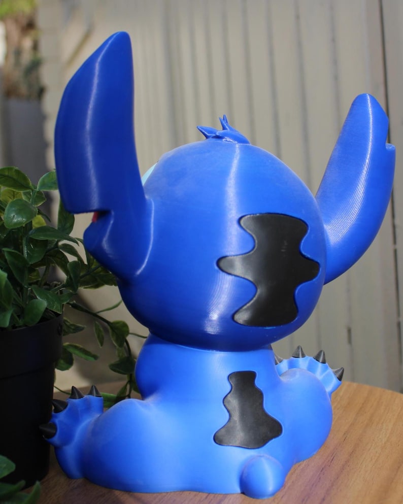 Puede incluir: Figura azul de Stitch, con grandes orejas, manchas negras y una espalda puntiaguda. La figura est&aacute; sentada, con una boca peque&ntilde;a y un dise&ntilde;o detallado. La figura es de pl&aacute;stico.