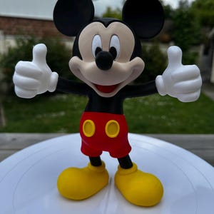K&ouml;nnte beinhalten: Eine Mickey Mouse-Figur, eine klassische Zeichentrickfigur, mit schwarzen Ohren, einem schwarzen K&ouml;rper und wei&szlig;en Handschuhen. Er tr&auml;gt rote Shorts mit gelben Kn&ouml;pfen und gelbe Schuhe und zeigt den Daumen nach oben.
