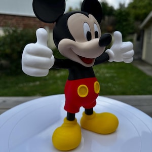 K&ouml;nnte beinhalten: Eine 3D-gedruckte Mickey Mouse-Figur. Die Figur hat schwarze Ohren, einen schwarzen Torso, rote Shorts mit gelben Kn&ouml;pfen, gelbe Schuhe und wei&szlig;e Handschuhe. Mickey hebt beide Daumen.
