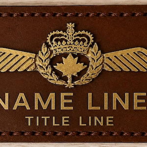 Peut inclure: Une étiquette de nom en cuir marron avec du texte et des ornements dorés. Le design comprend une couronne, des ailes, une feuille d'érable et les mots "NAME LINE" et "TITLE LINE". Les bords sont cousus.