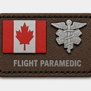 May include: A rectangular brown leather patch with rounded corners and black stitching. It features a Canadian flag, a silver-colored Star of Life emblem with a serpent-entwined staff, and the text FLIGHT PARAMEDIC printed in silver lettering.