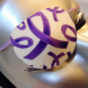 Peut inclure: Un cache-œil blanc avec un motif de ruban violet. Le cache-œil est porté sur une tête de mannequin.