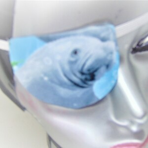 May include: A blue eye patch with a close-up image of a manatee. The manatee is facing the left side of the image. The eye patch is made of soft fabric and has an elastic strap.