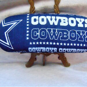 以下が含まれることがあります： 「COWBOYS」という文字が複数回印刷された青と白の布製の眼鏡ケース。ケースは白い星で飾られています。