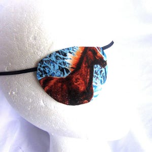 May include: A blue and brown eye patch with a horse design. The horse is brown with a white mane and tail. The background is a blue and white winter scene.
