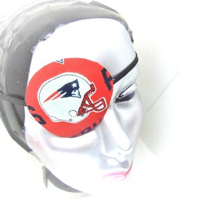 以下が含まれることがあります： フットボールのヘルメットとニューイングランド・ペイトリオッツのロゴがついた赤と白のアイパッチ。アイパッチはマネキンの頭につけられています。