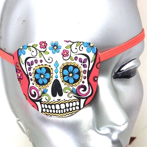May include: A red, white and blue sugar skull eye patch with an elastic band. The eye patch is decorated with floral designs.