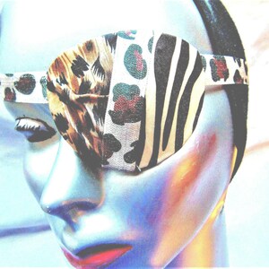 May include: A close-up of a person wearing a black and white zebra print eye patch with a leopard print and floral pattern. The eye patch is made of fabric and has a black elastic strap.