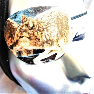 May include: A brown and white wolf eye patch with a blue and black background. The eye patch is made of fabric and has a black elastic strap.