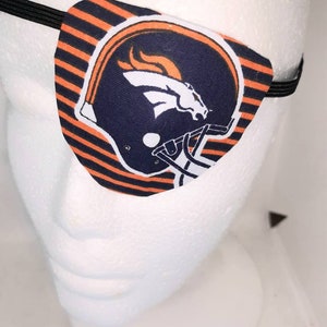 Può includere: Un paraluce a strisce nere e arancioni con il logo dei Denver Broncos. Il logo è una testa di cavallo bianca con una fiamma arancione dietro, all'interno di un casco blu.