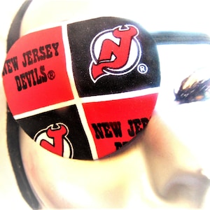 May include: A red, black, and white eye patch with the New Jersey Devils logo. The logo is a red and white stylized "N" with a red devil's tail.