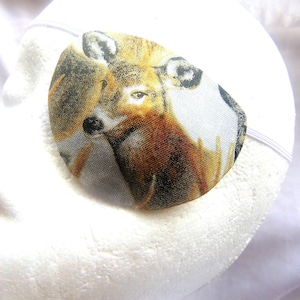 May include: A white eye patch with a printed image of a deer with brown and white fur. The deer is looking to the left.
