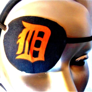 May include: A black eye patch with an orange "D" on it. The eye patch is made of fabric and has an elastic strap.