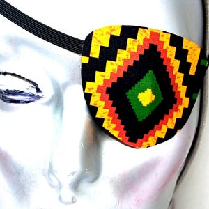May include: A black eye patch with a colorful geometric pattern in red, yellow, green, and orange. The eye patch is made of fabric and has an elastic band.