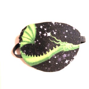 May include: A green dragon eye patch with a black background and white stars. The eye patch has an elastic strap.