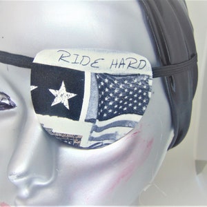 May include: A black and white eye patch with a star and American flag design. The eye patch has an elastic strap and says "RIDE HARD" in black lettering.