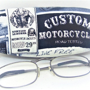 May include: A black and white fabric eyeglass case with the text "CUSTOM MOTORCYCLES ROAD TESTED LIVE FREE" and a vintage motorcycle jacket advertisement.