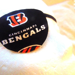 Puede incluir: Parche para el ojo negro con el logotipo de los Cincinnati Bengals y el nombre del equipo en letras blancas.