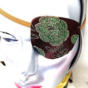 May include: A brown eye patch with a green floral pattern. The eye patch is made of fabric and has an elastic band.