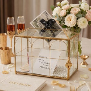 May include: A rectangular glass card box with a gold metal frame, featuring a heart-shaped padlock. Inside, a white card displays the text 'Believe! And the impossible becomes possible!'. The box is decorated with white pearls and a black ribbon.