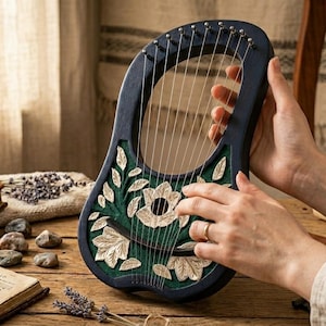 May include: A dark blue lyre with a green and cream floral design. The instrument has strings and is held by a person. A book titled "Harmony Herald" and sheet music are on a wooden surface.