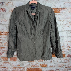 May include: A gray blazer with vertical pinstripes, featuring a notched collar and three-button closure. The Ann Taylor brand label is visible. The jacket is hanging on a pink hanger against a brick wall.