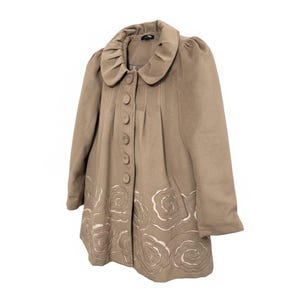 May include: A tan-colored coat with a large, rounded collar and decorative floral embroidery along the hemline. The coat features a row of large buttons down the front and a slightly flared silhouette.
