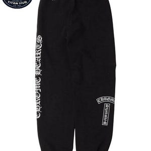 May include: Black sweatpants with white "CHROME HEARTS" lettering down the left leg and on the right leg. The text "Fuck You" is printed on the upper back. The sweatpants have a drawstring waist and elastic cuffs.