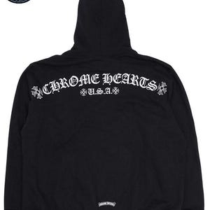 May include: Black hooded sweatshirt with the text "CHROME HEARTS U.S.A." in white script across the back. The sweatshirt has a drawstring hood and a kangaroo pocket. The Chrome Hearts logo is visible on the back.