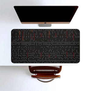 May include: Overhead view of a modern desk setup featuring a black computer monitor, a black desk mat with a grid pattern of white dots and red lines, and a brown office chair. The desk is white.